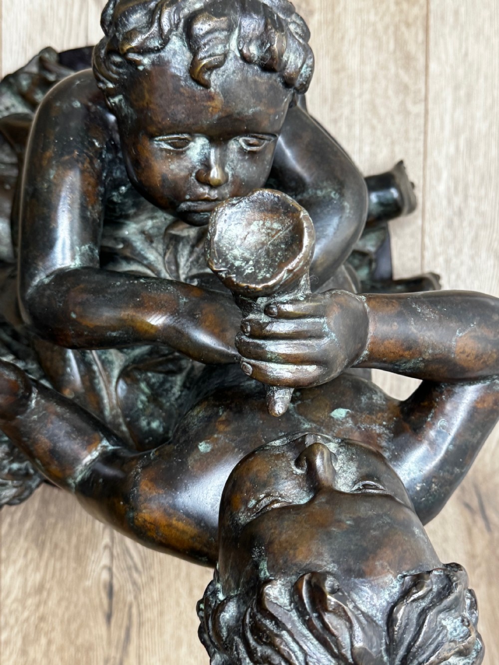 A dark patinated French bronze sculptural group depicting three putti playing, with one child blowing into a conch shell. View XXIV