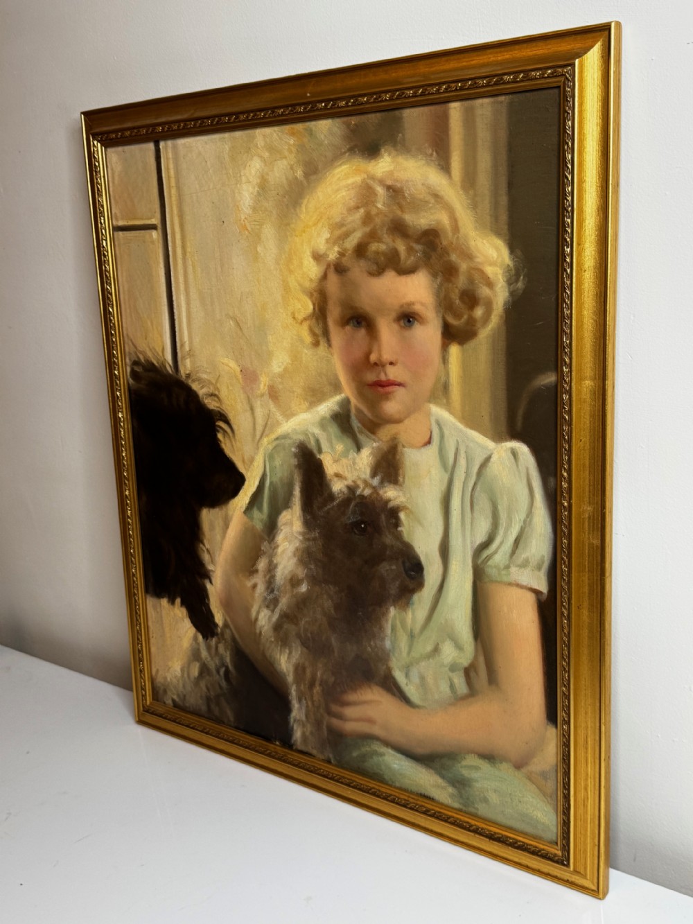 A mid-20th-century oil portrait depicting a young girl with blonde curly hair holding a Cairn Terrier. View IX