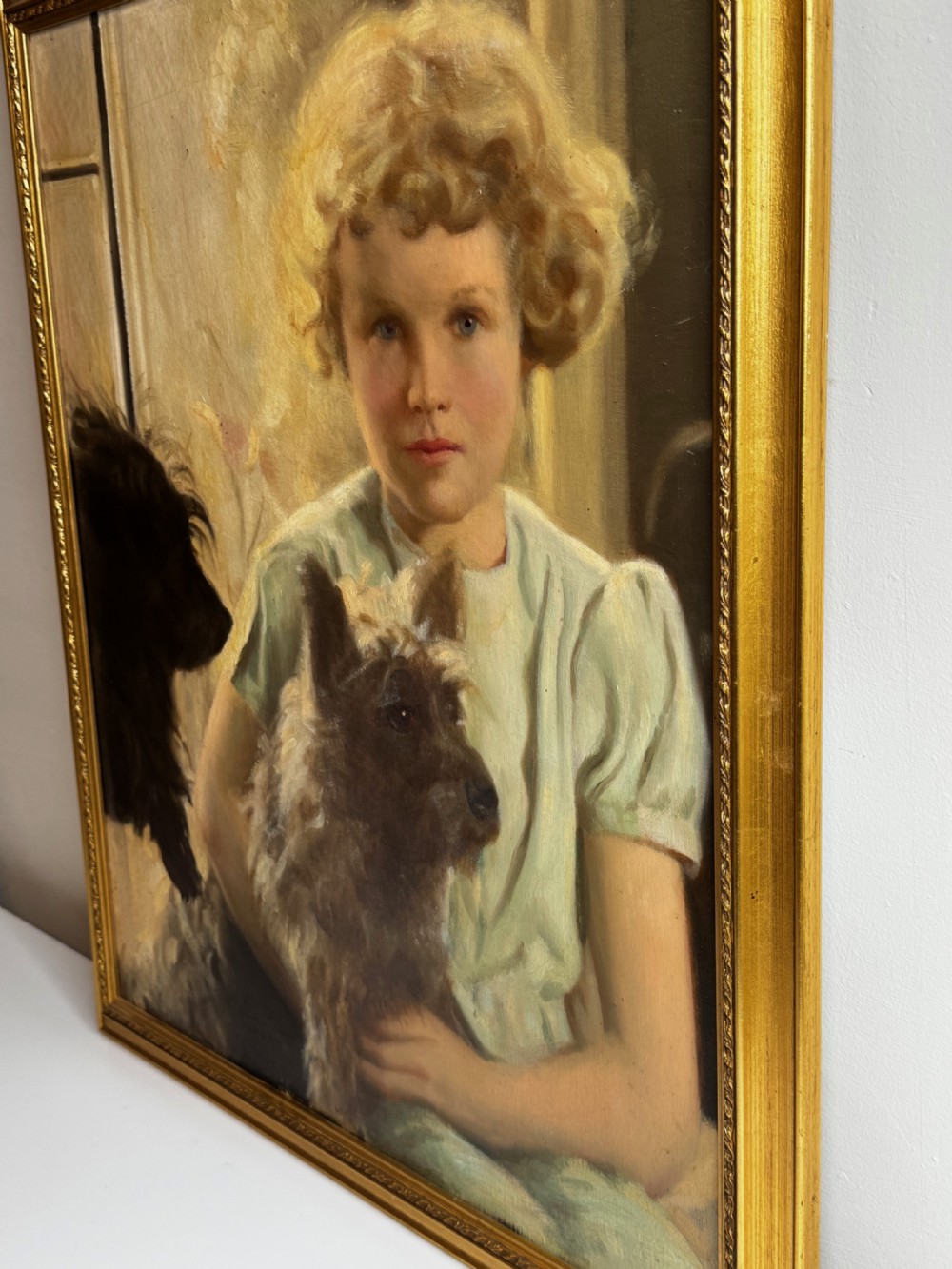 A mid-20th-century oil portrait depicting a young girl with blonde curly hair holding a Cairn Terrier. View X