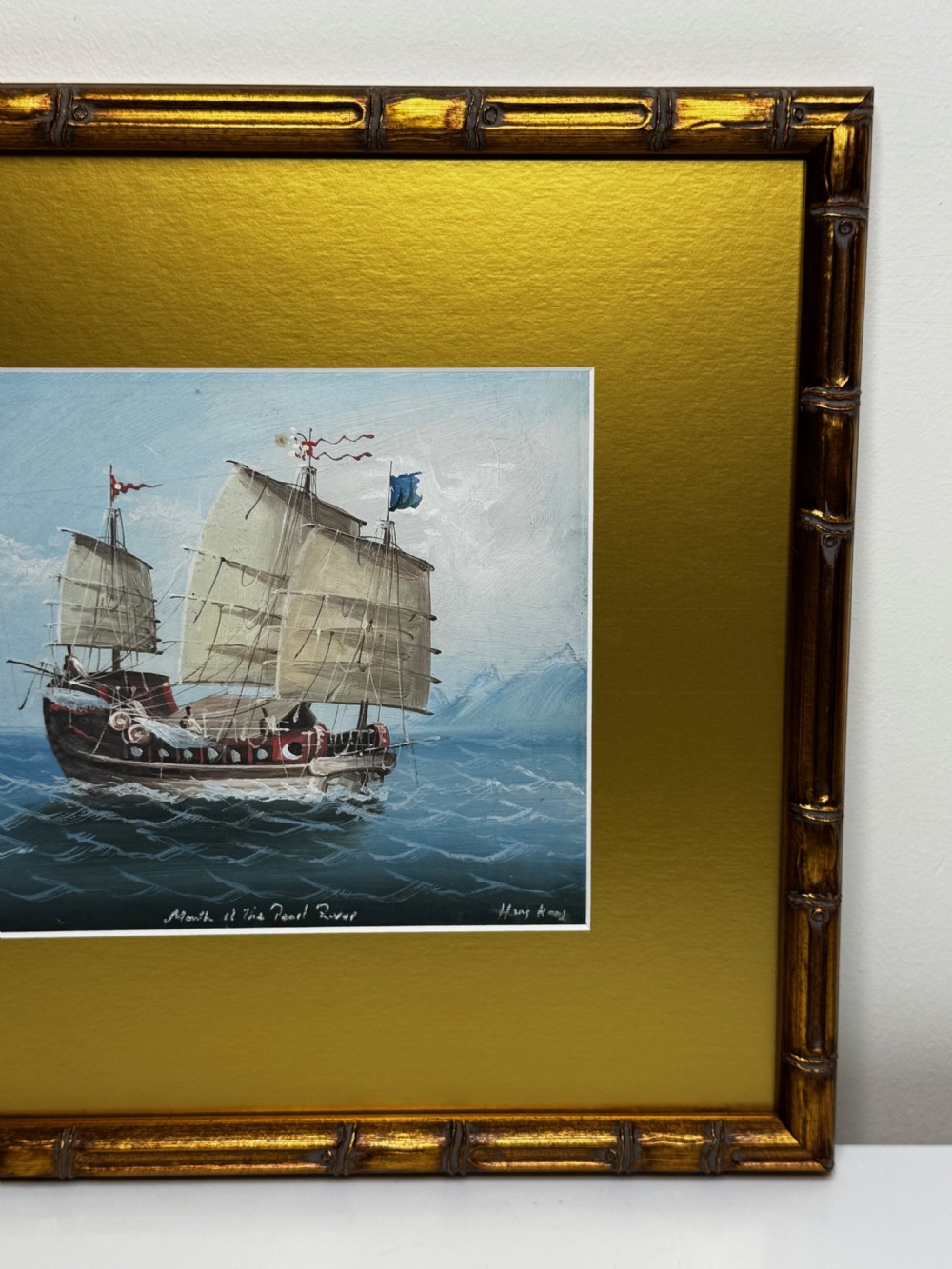 An antique oil painting depicting a Chinese junk ship sailing on blue water, set within a wide gold mount and a gilt faux-bamboo frame. View XXX