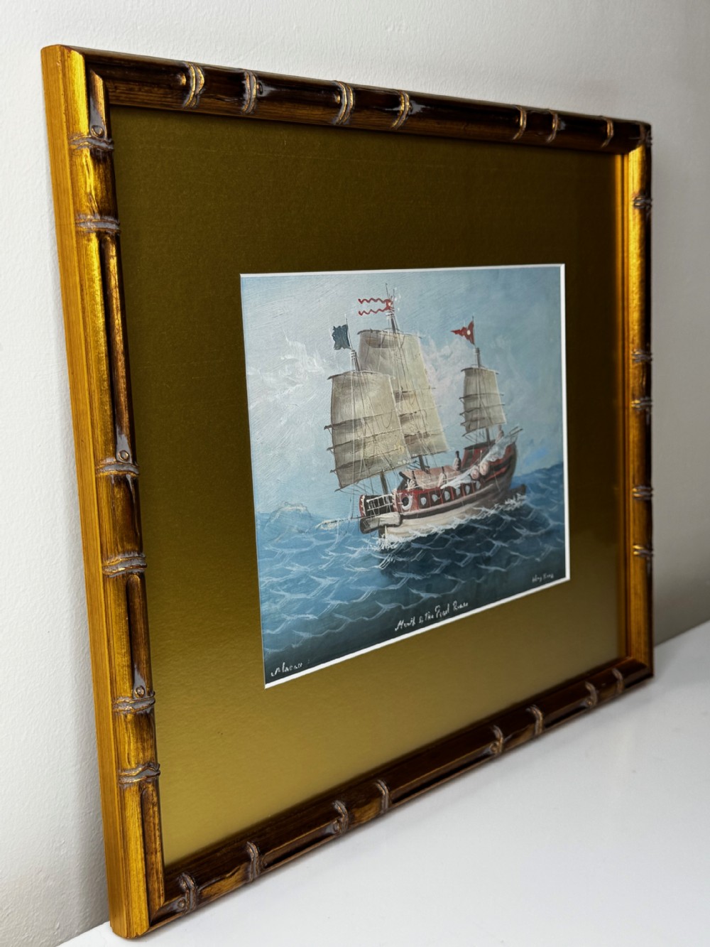 A framed marine painting depicting a Chinese junk ship navigating blue waters under a light sky, presented within a wide gold mount and a gilt faux bamboo frame. View XXVIII