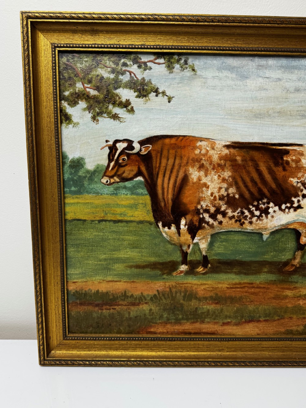 A 19th-century oil painting depicting a brown and white shorthorn bull standing in side profile in a green field, encased in a gilded frame. View III