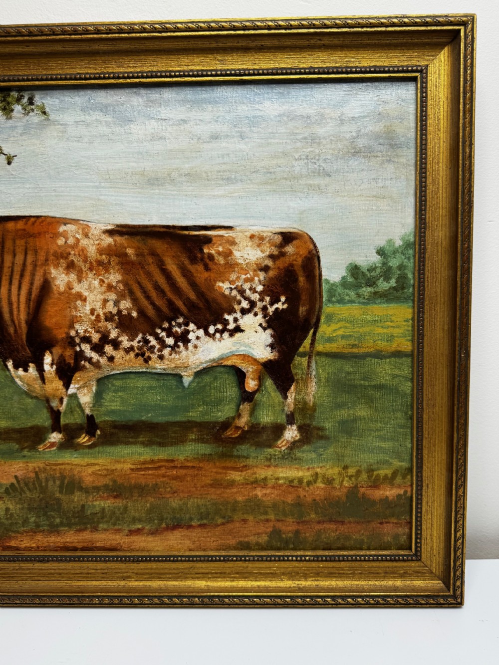 A 19th-century oil painting depicting a brown and white shorthorn bull standing in side profile in a green field, encased in a gilded frame. View VIII