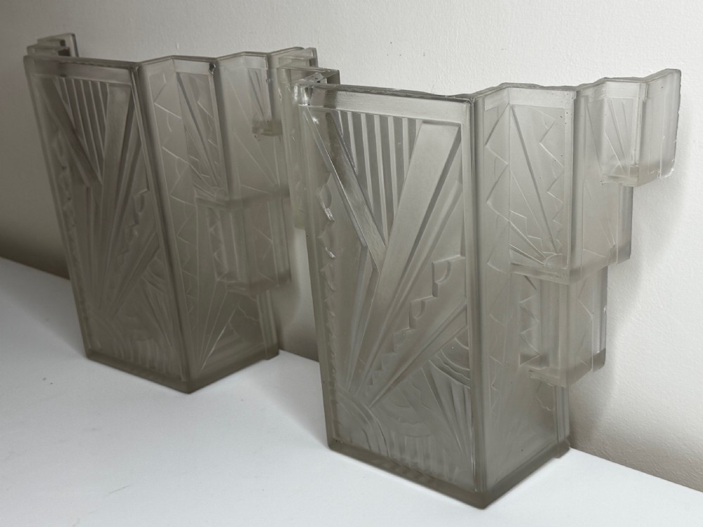 A pair of Art Deco frosted moulded glass wall lights featuring a stepped skyscraper silhouette with geometric sunburst and chevron carvings. View VII