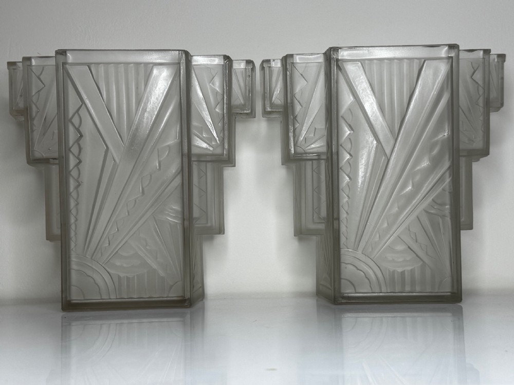 A pair of Art Deco frosted moulded glass wall lights featuring a stepped skyscraper silhouette with geometric sunburst and chevron carvings. View XIII
