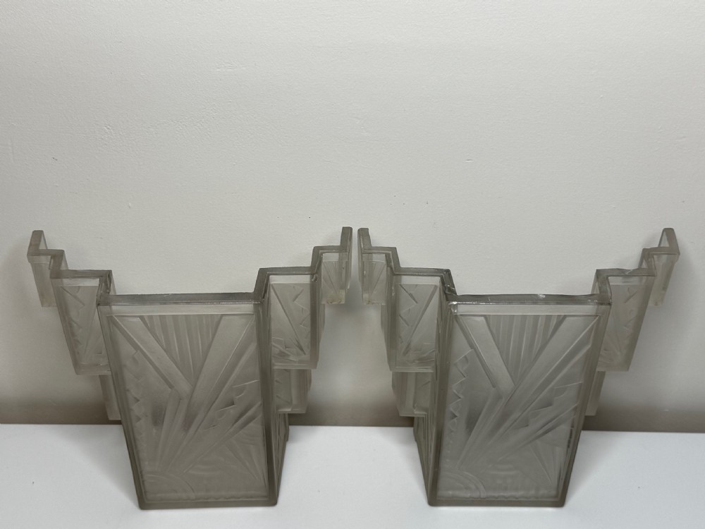 A pair of Art Deco frosted moulded glass wall lights featuring a stepped skyscraper silhouette with geometric sunburst and chevron carvings. View XV