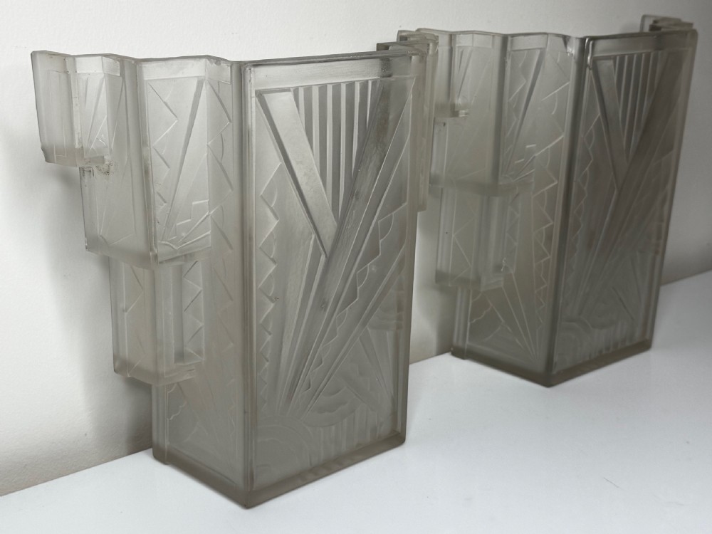 A pair of Art Deco frosted moulded glass wall lights featuring a stepped skyscraper silhouette with geometric sunburst and chevron carvings. View XVI