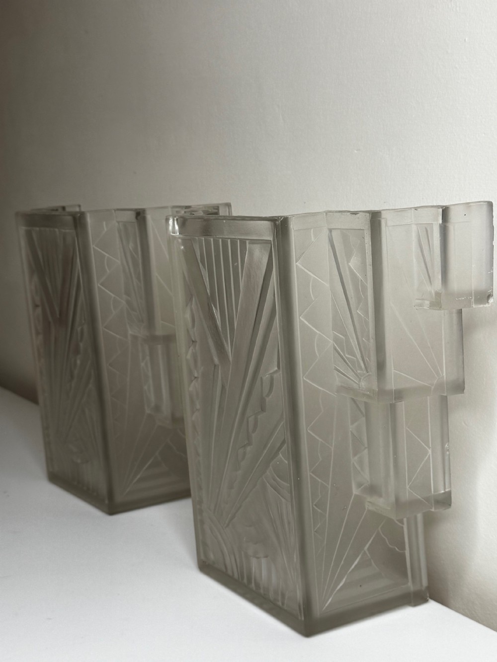 A pair of Art Deco frosted moulded glass wall lights featuring a stepped skyscraper silhouette with geometric sunburst and chevron carvings. View XVIII