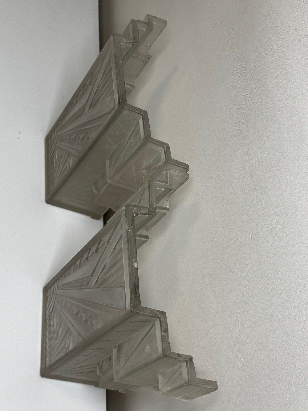 A pair of Art Deco frosted moulded glass wall lights featuring a stepped skyscraper silhouette with geometric sunburst and chevron carvings. View XIX
