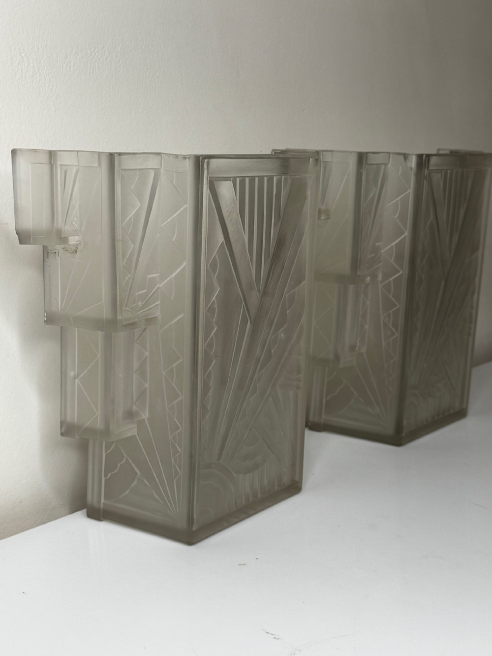 A pair of Art Deco frosted moulded glass wall lights featuring a stepped skyscraper silhouette with geometric sunburst and chevron carvings. View XX