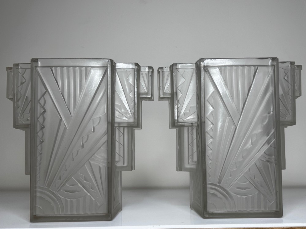 A pair of Art Deco frosted moulded glass wall lights featuring a stepped skyscraper silhouette with geometric sunburst and chevron carvings. View XXI