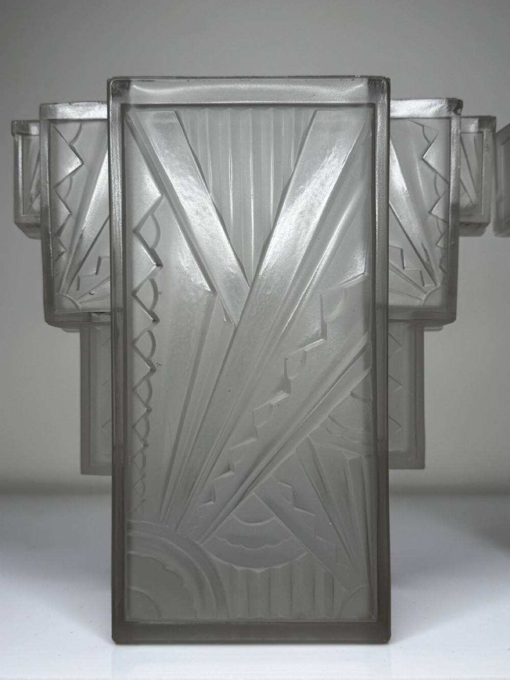 A pair of Art Deco frosted moulded glass wall lights featuring a stepped skyscraper silhouette with geometric sunburst and chevron carvings. View XXII
