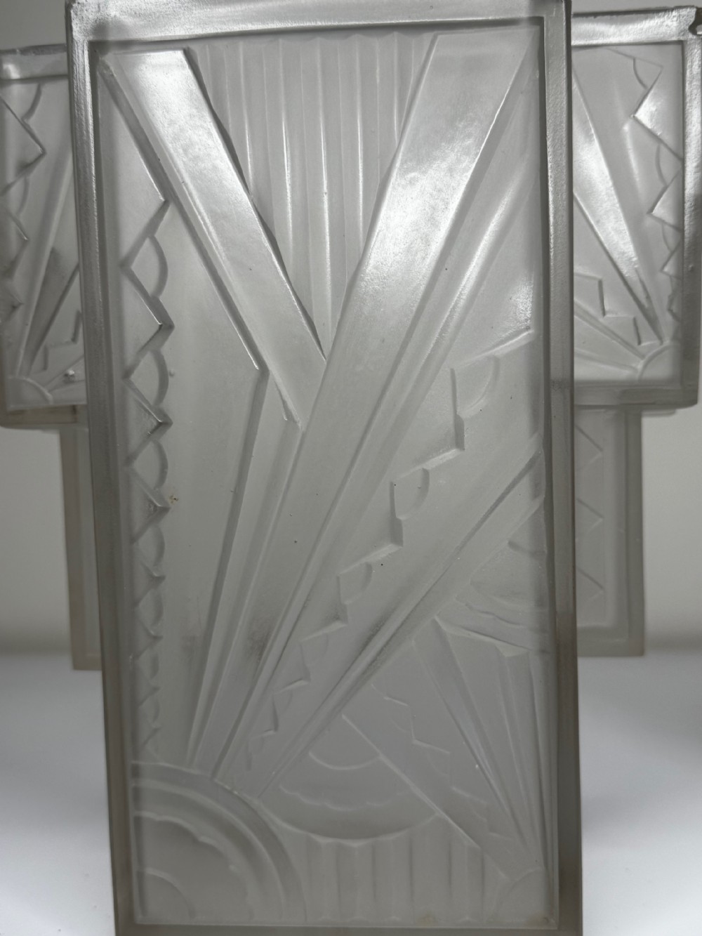 A pair of Art Deco frosted moulded glass wall lights featuring a stepped skyscraper silhouette with geometric sunburst and chevron carvings. View XXV