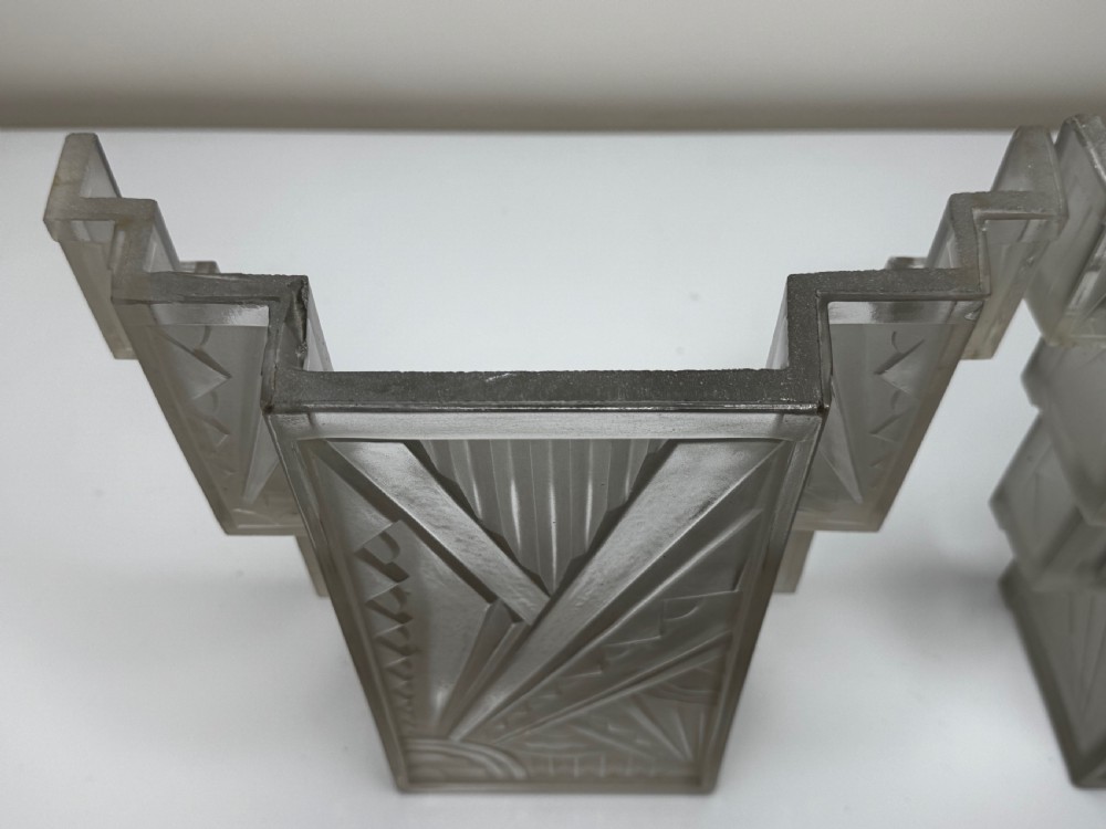 A pair of Art Deco frosted moulded glass wall lights featuring a stepped skyscraper silhouette with geometric sunburst and chevron carvings. View XXVIII