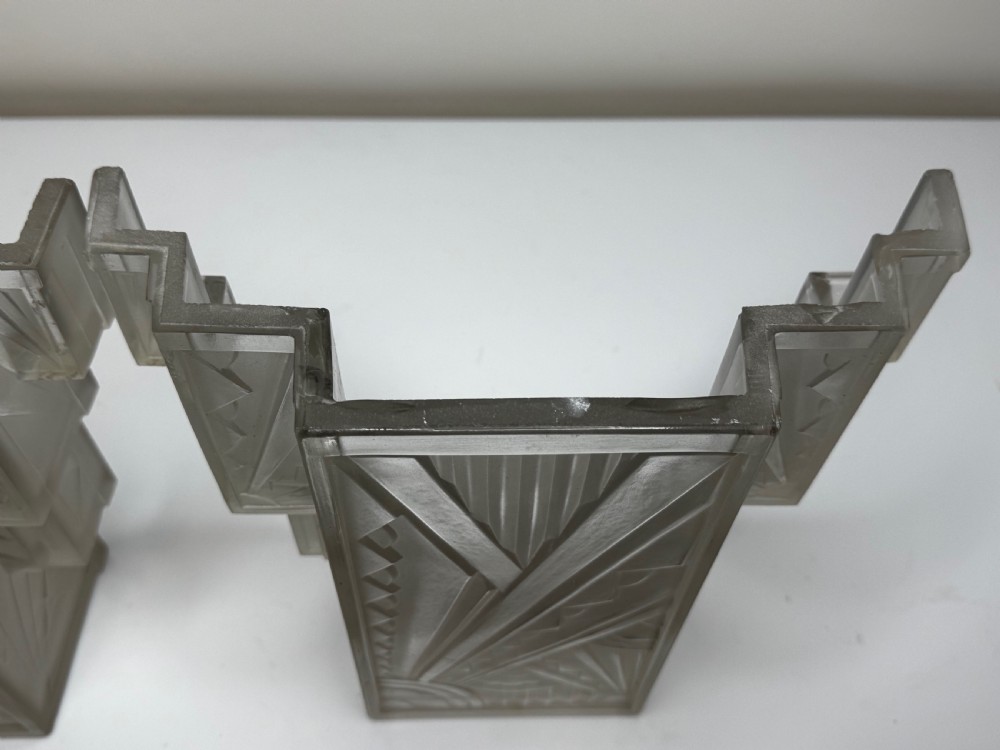 A pair of Art Deco frosted moulded glass wall lights featuring a stepped skyscraper silhouette with geometric sunburst and chevron carvings. View XXIX