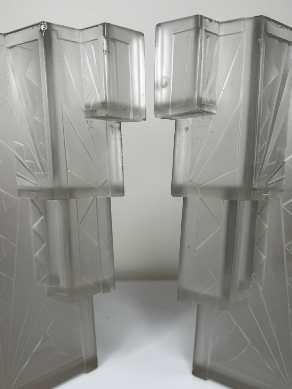 A pair of Art Deco frosted moulded glass wall lights featuring a stepped skyscraper silhouette with geometric sunburst and chevron carvings. View XXXI