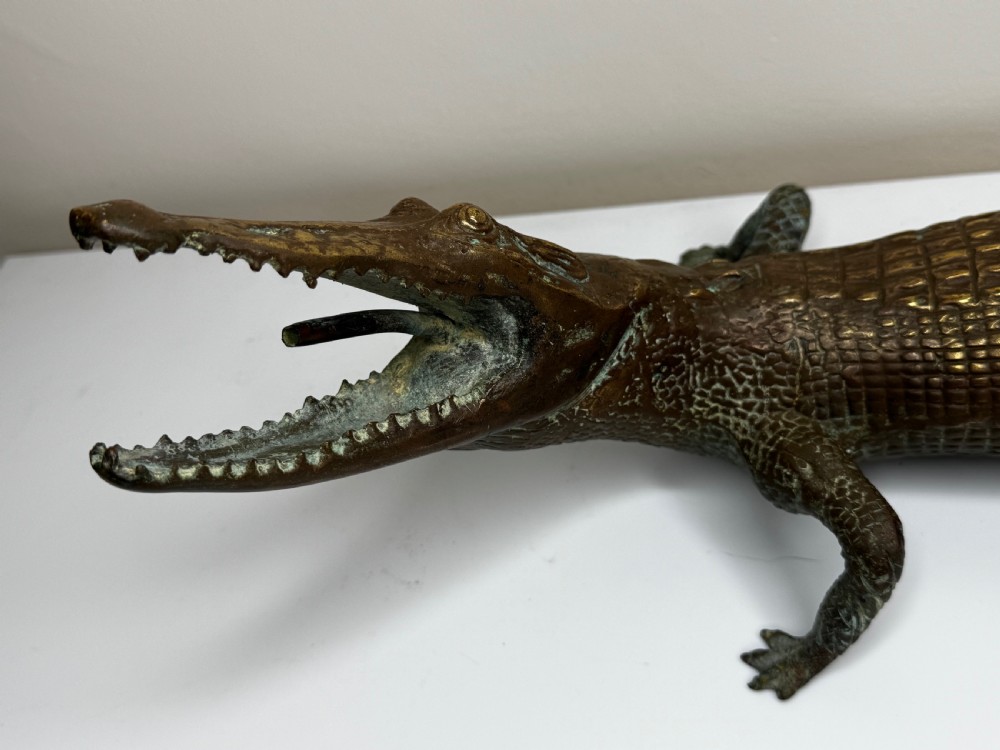 A dark bronze sculpture of a crocodile with an open mouth, detailed scales, and a curved tail designed as a water fountain spout. View V