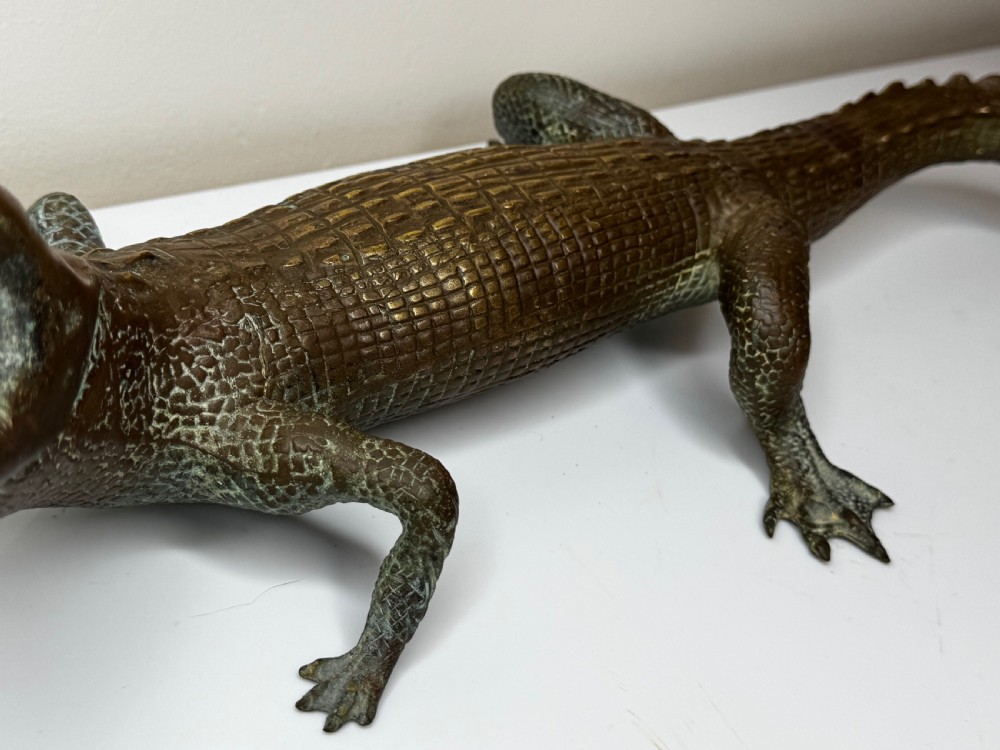 A dark bronze sculpture of a crocodile with an open mouth, detailed scales, and a curved tail designed as a water fountain spout. View XIII