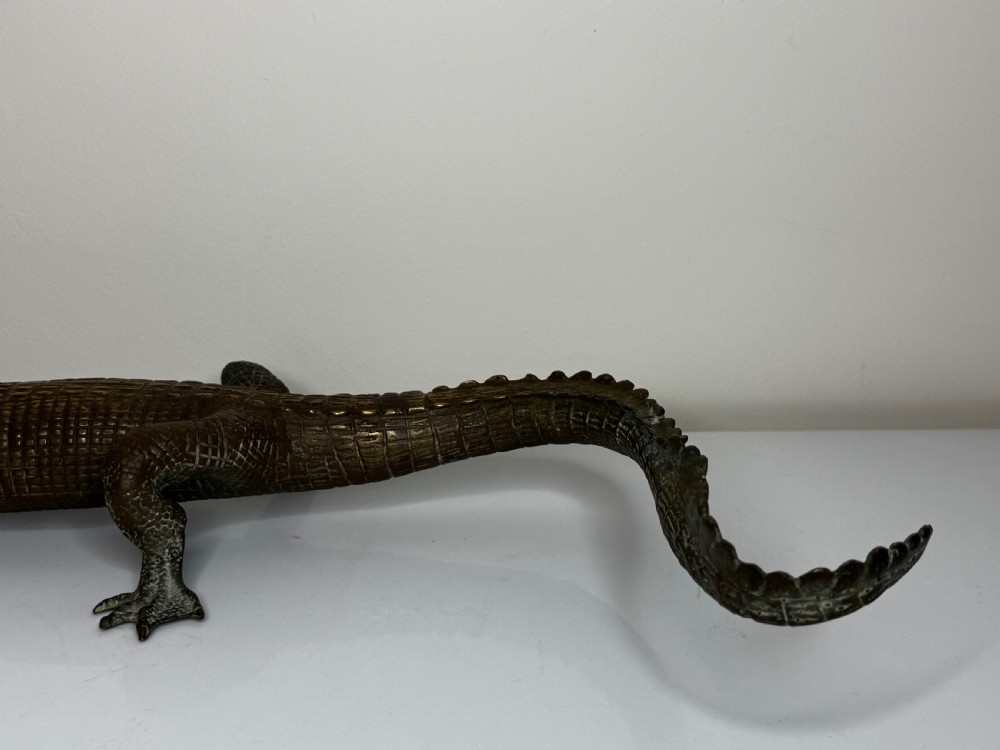 A dark bronze sculpture of a crocodile with an open mouth, detailed scales, and a curved tail designed as a water fountain spout. View XV