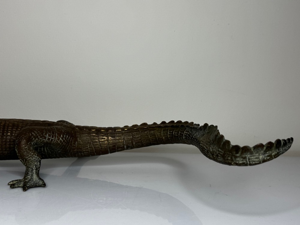 A dark bronze sculpture of a crocodile with an open mouth, detailed scales, and a curved tail designed as a water fountain spout. View XVI