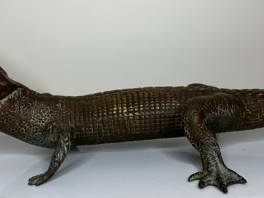 A dark bronze sculpture of a crocodile with an open mouth, detailed scales, and a curved tail designed as a water fountain spout. View XVIII