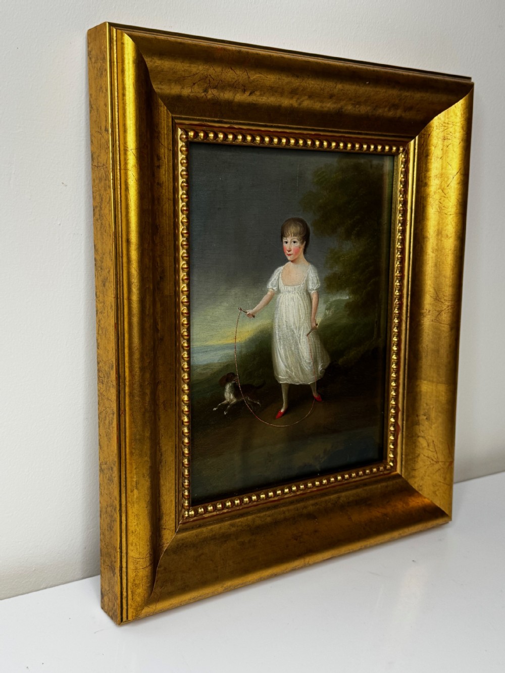 A Georgian oil painting depicted in an ornate gilded frame shows a young girl in a white dress holding a skipping rope alongside a dog in a rural landscape. View III