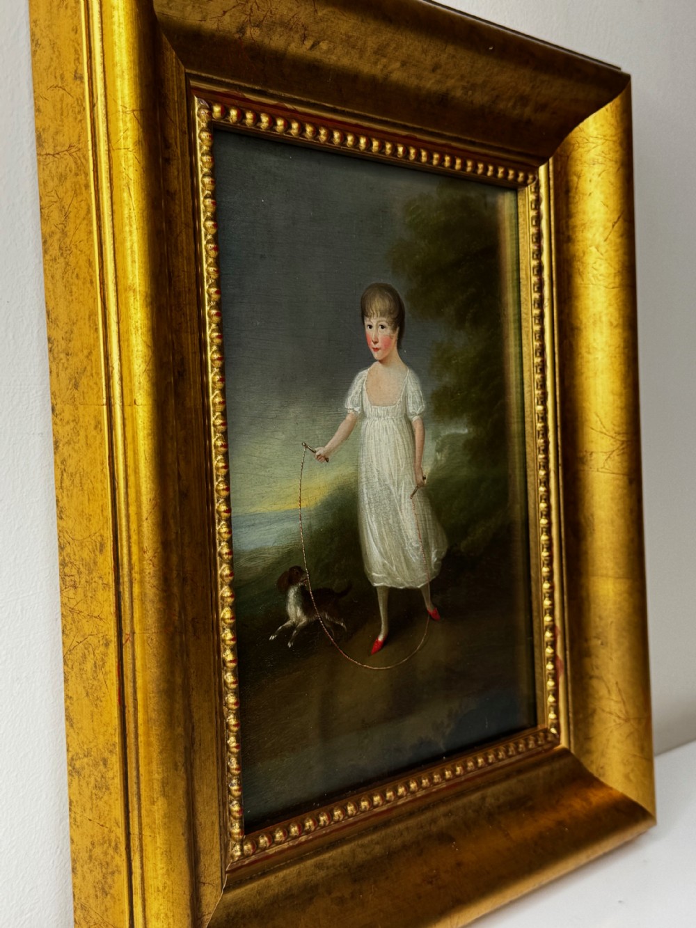 A Georgian oil painting depicted in an ornate gilded frame shows a young girl in a white dress holding a skipping rope alongside a dog in a rural landscape. View IV