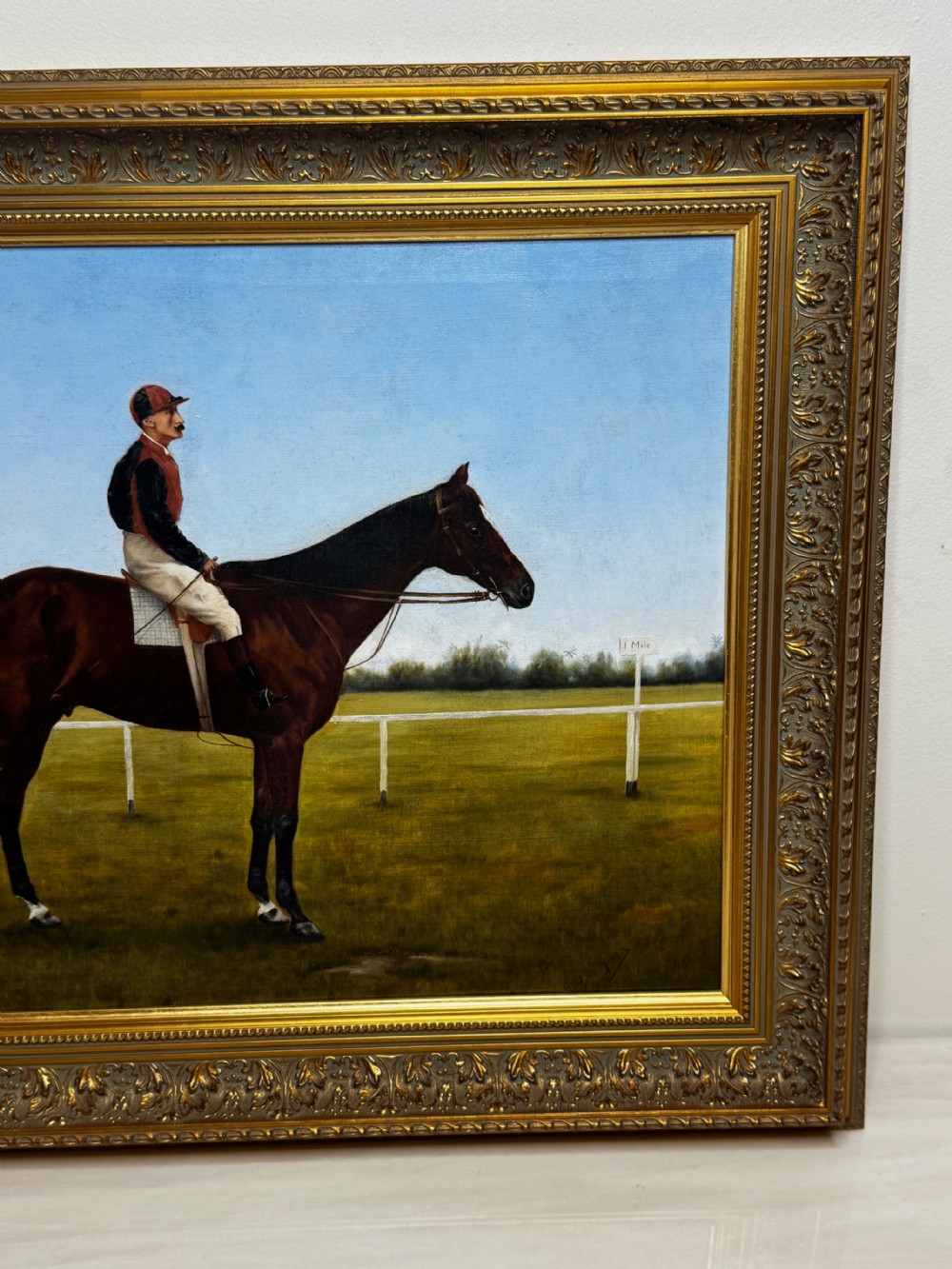 A framed Victorian oil painting depicting a bay racehorse and mounted jockey against a blue sky and green racecourse backdrop. View II