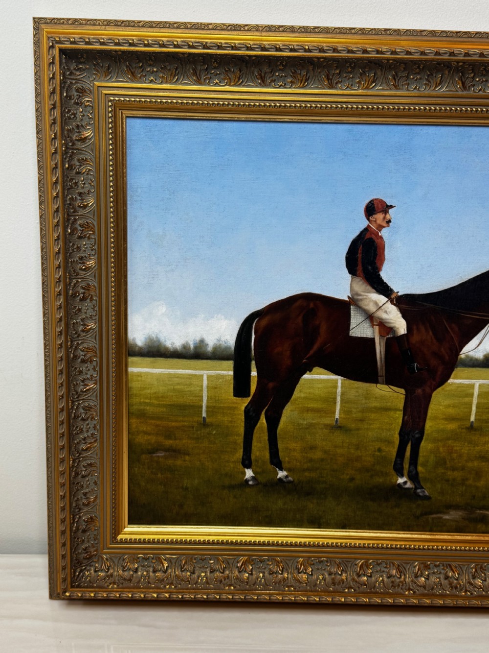 A framed Victorian oil painting depicting a bay racehorse and mounted jockey against a blue sky and green racecourse backdrop. View VII
