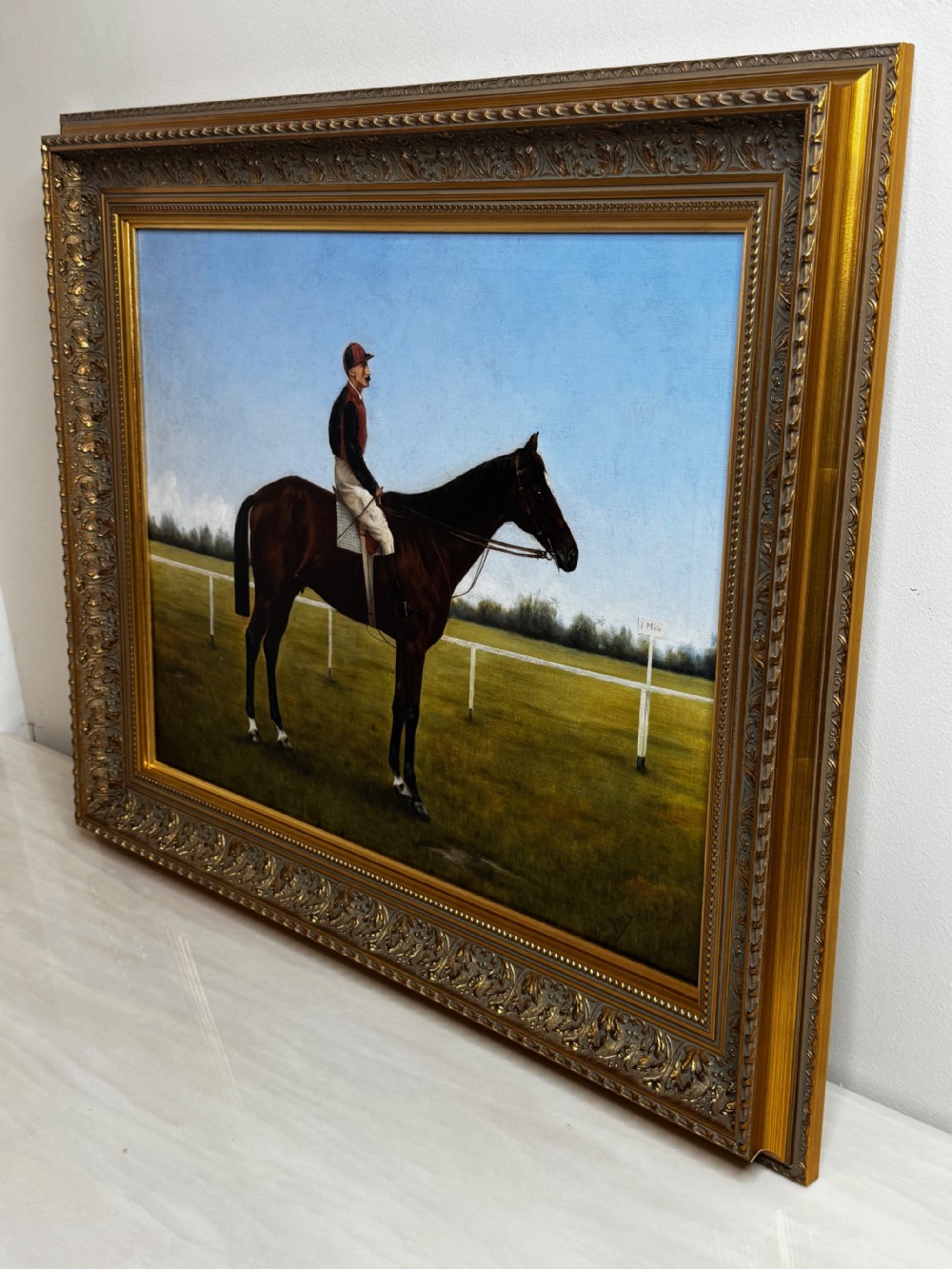 A framed Victorian oil painting depicting a bay racehorse and mounted jockey against a blue sky and green racecourse backdrop. View VIII