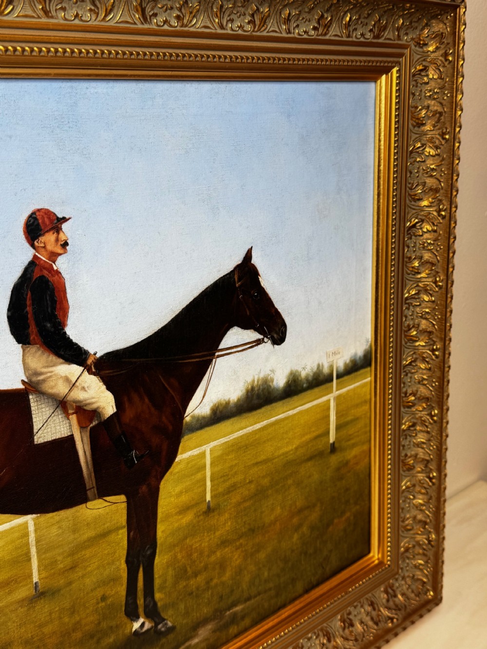 A framed Victorian oil painting depicting a bay racehorse and mounted jockey against a blue sky and green racecourse backdrop. View XI