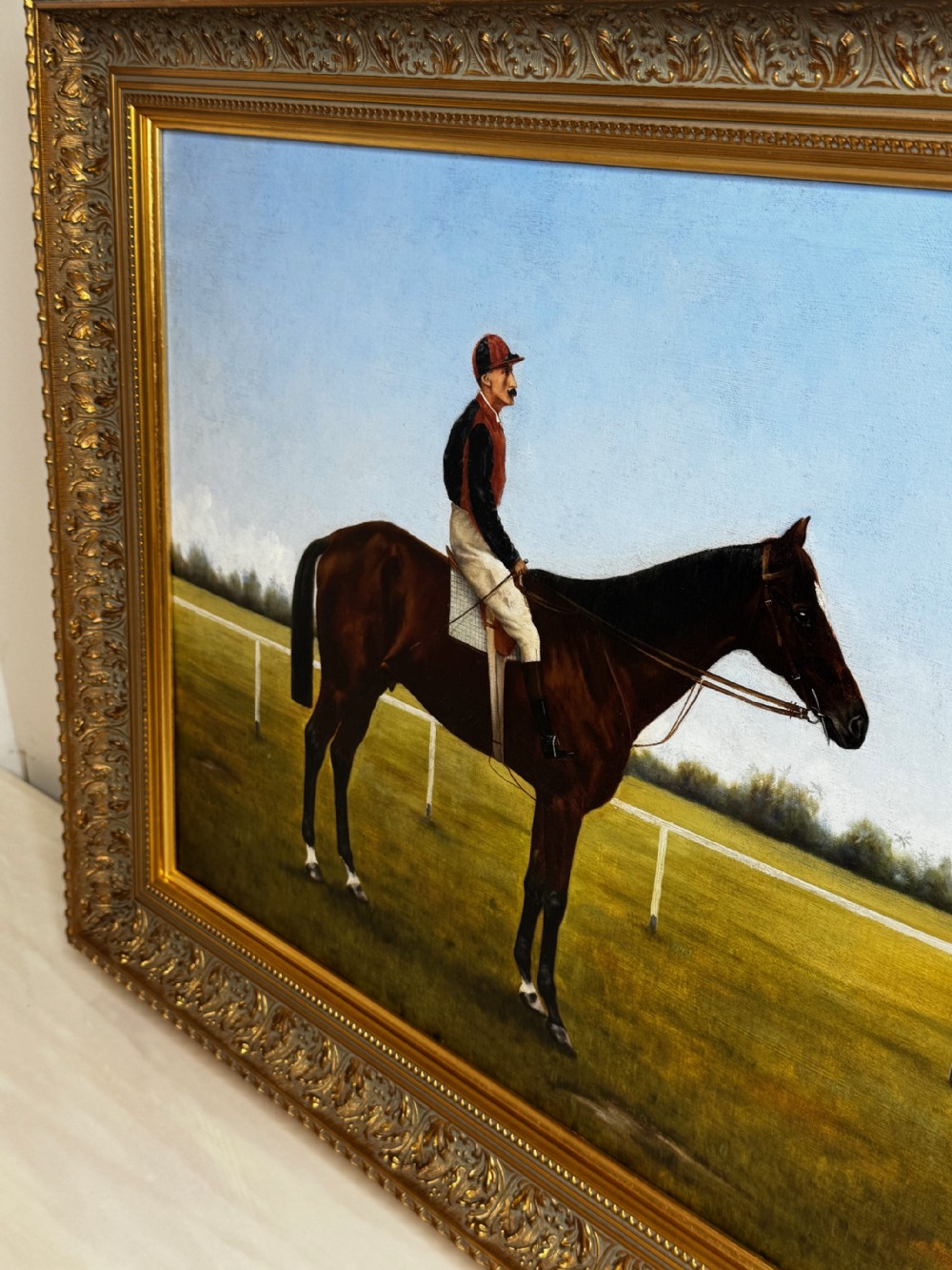 A framed Victorian oil painting depicting a bay racehorse and mounted jockey against a blue sky and green racecourse backdrop. View XII