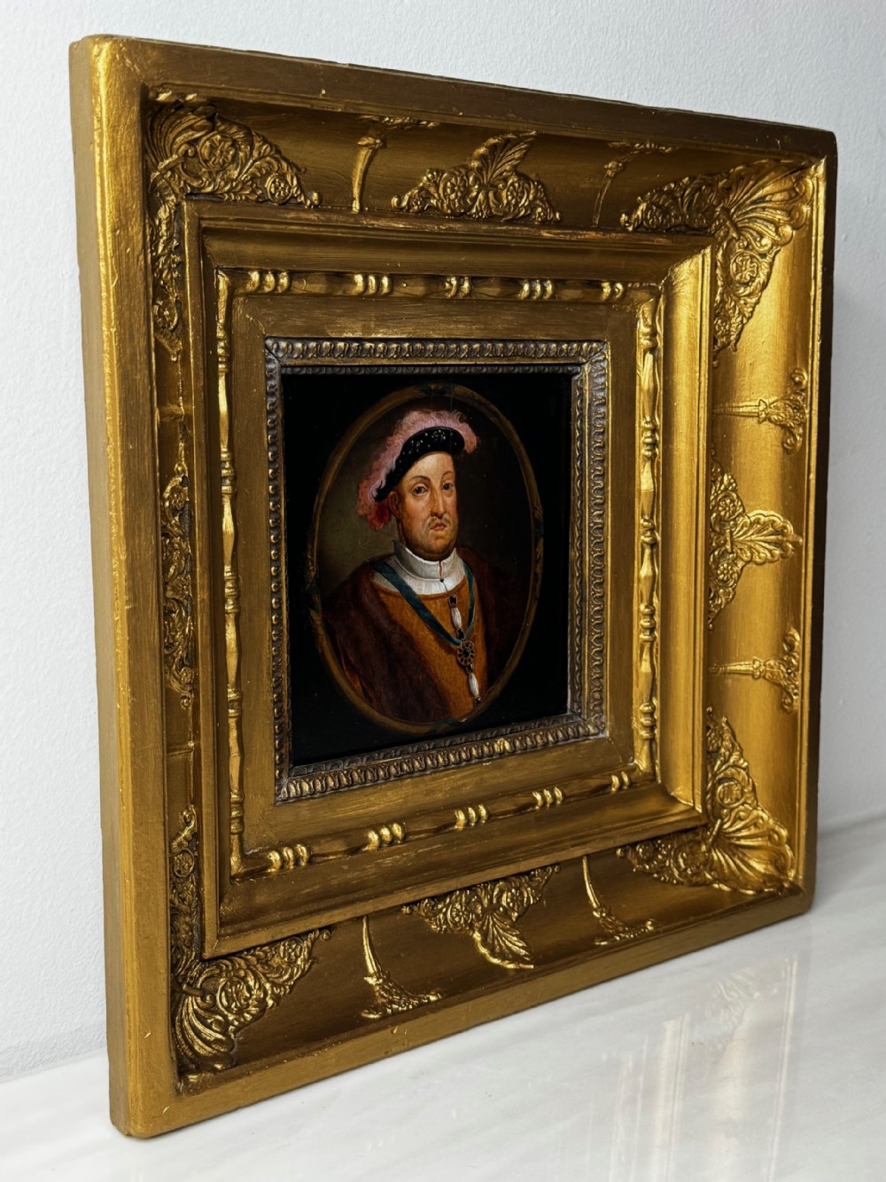 An oval oil portrait of King Henry VIII wearing the Order of the Garter badge, enclosed in a heavily ornate gilded wooden frame. View VII