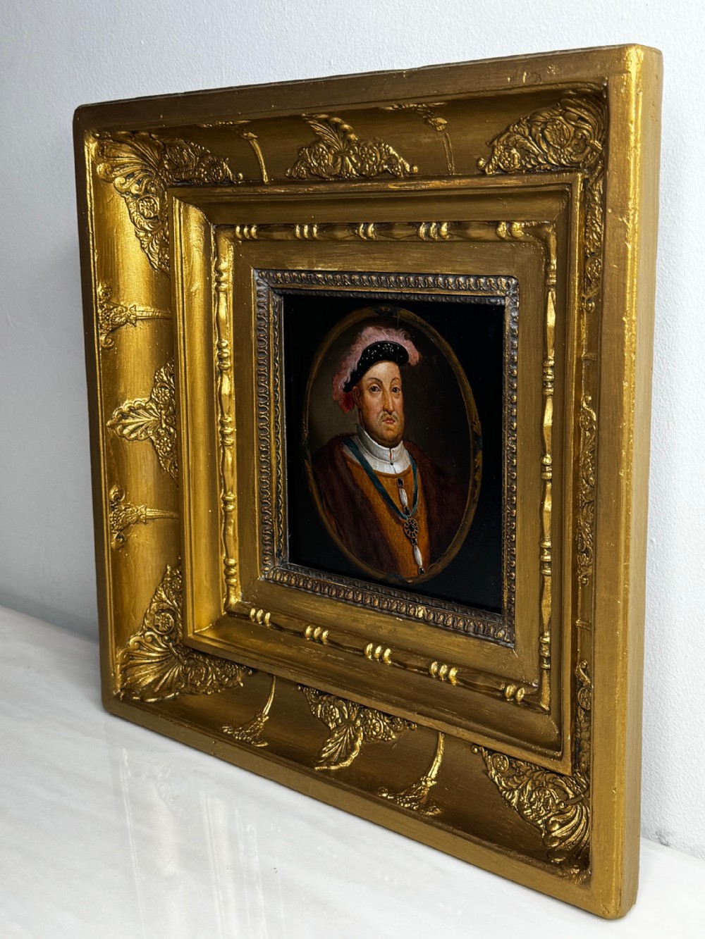 An oval oil portrait of King Henry VIII wearing the Order of the Garter badge, enclosed in a heavily ornate gilded wooden frame. View IX