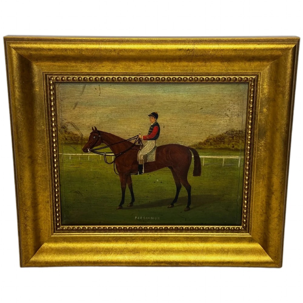 An oil painting depicting a brown thoroughbred racehorse with a jockey in red and blue silks, set within a wide gilded frame.
