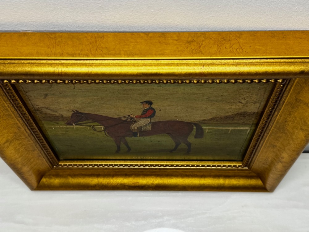An oil painting depicting a brown thoroughbred racehorse with a jockey in red and blue silks, set within a wide gilded frame. View III