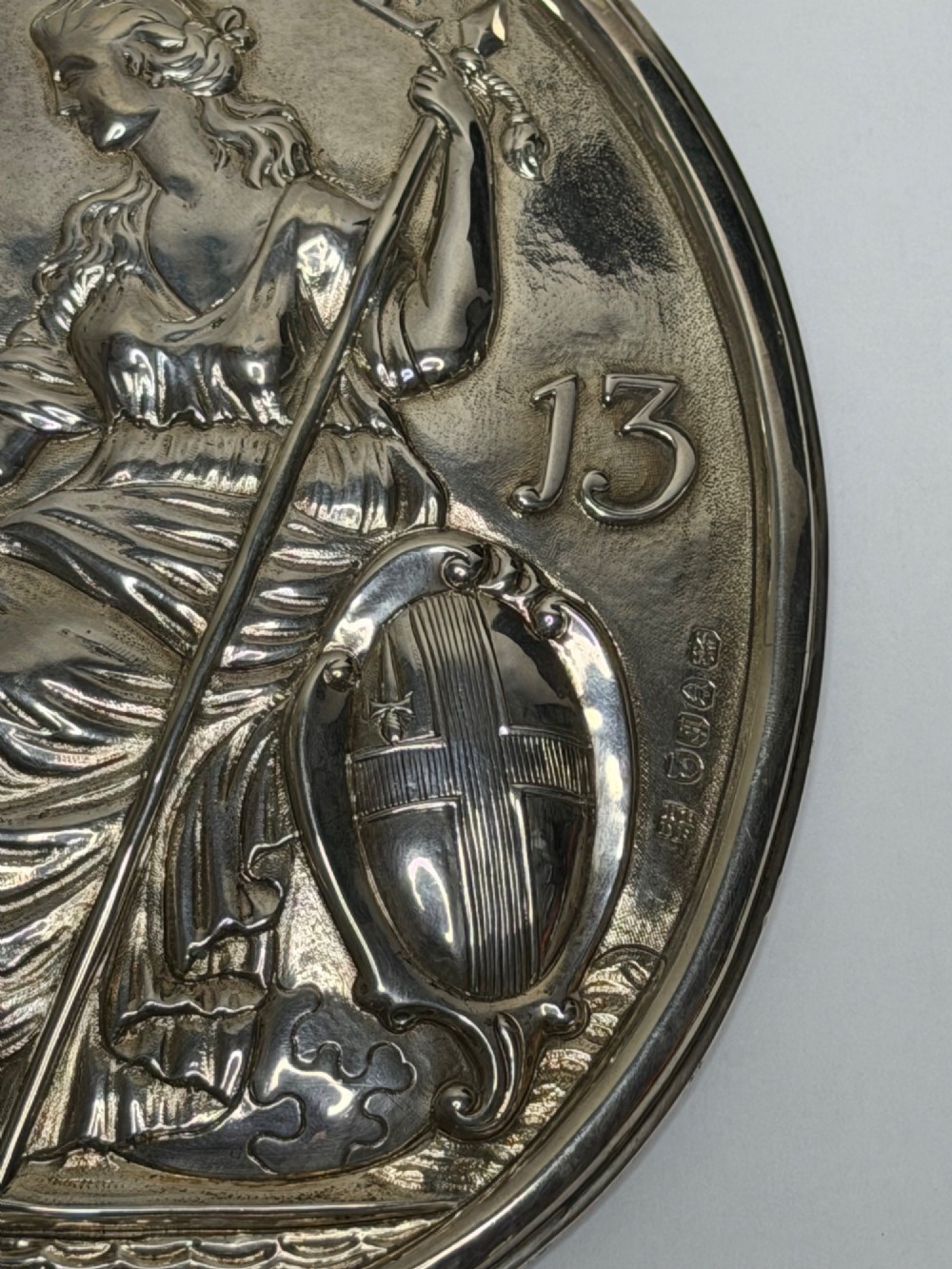 An oval George III sterling silver plaque featuring an embossed relief of Britannia holding a spear beside a shield and harp with embossed text reading London Assurance. View II
