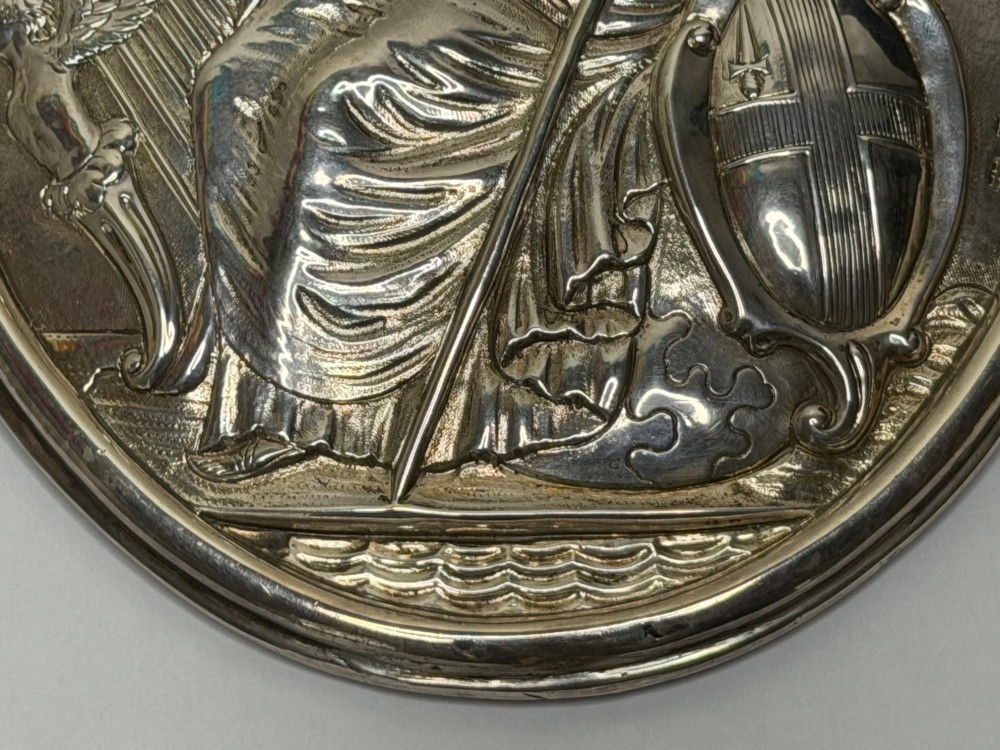 An oval George III sterling silver plaque featuring an embossed relief of Britannia holding a spear beside a shield and harp with embossed text reading London Assurance. View V