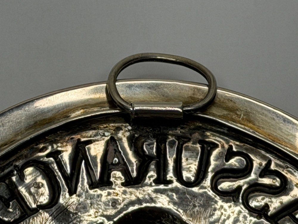 An oval George III sterling silver plaque featuring an embossed relief of Britannia holding a spear beside a shield and harp with embossed text reading London Assurance. View X