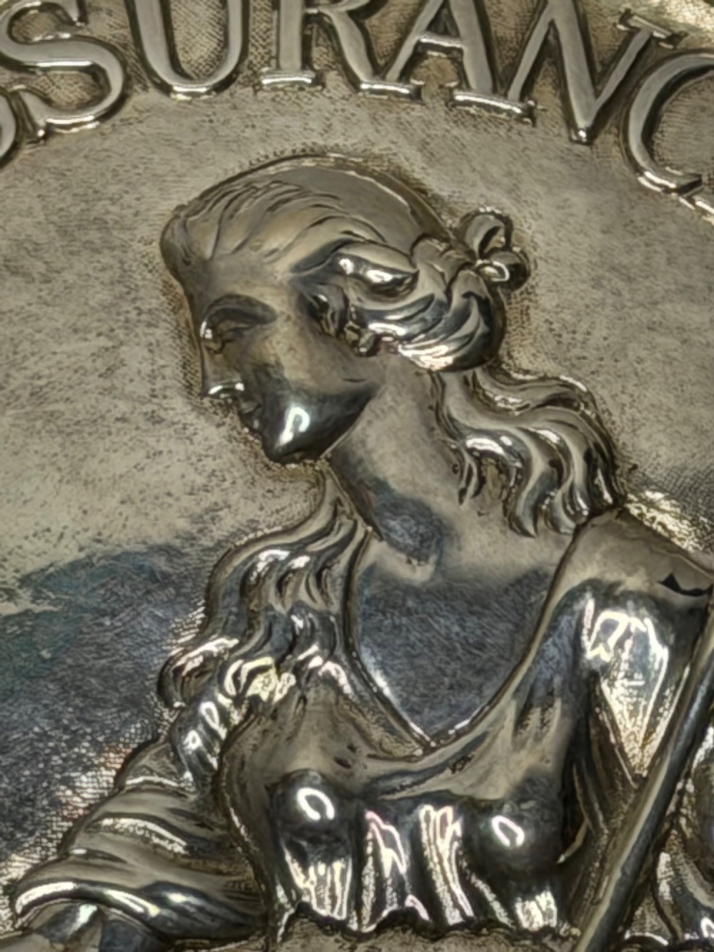 An oval George III sterling silver plaque featuring an embossed relief of Britannia holding a spear beside a shield and harp with embossed text reading London Assurance. View XIII
