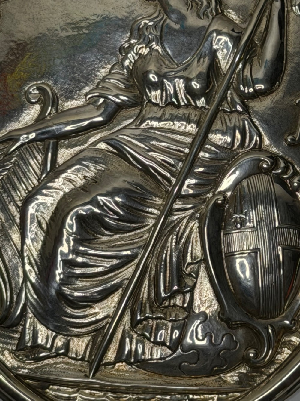 An oval George III sterling silver plaque featuring an embossed relief of Britannia holding a spear beside a shield and harp with embossed text reading London Assurance. View XV