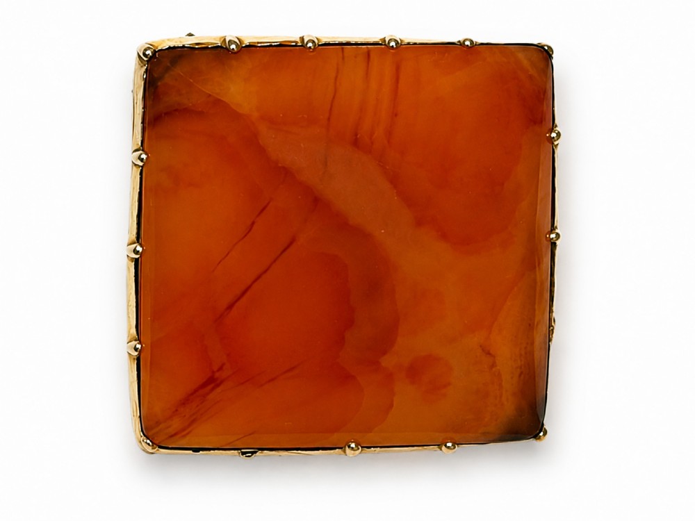 A square-cut translucent warm orange carnelian agate gemstone held in a 9ct gold frame with claw settings.