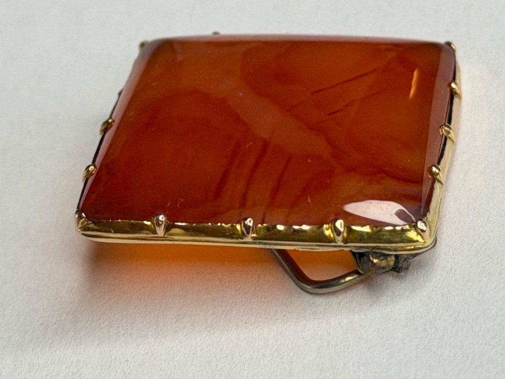 A square-cut translucent warm orange carnelian agate gemstone held in a 9ct gold frame with claw settings. View IV