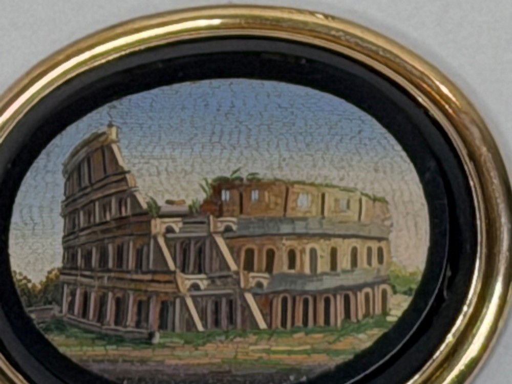 An oval nineteenth-century micromosaic brooch set in a yellow gold bezel depicting the Roman Colosseum against a light blue sky within a black surround. View II