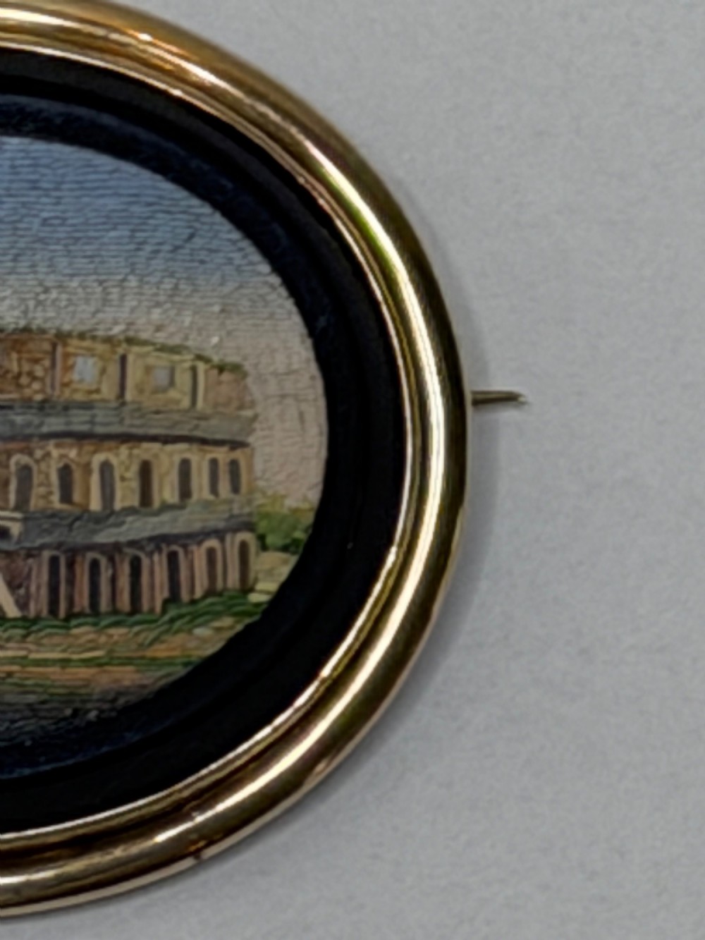 An oval nineteenth-century micromosaic brooch set in a yellow gold bezel depicting the Roman Colosseum against a light blue sky within a black surround. View IV