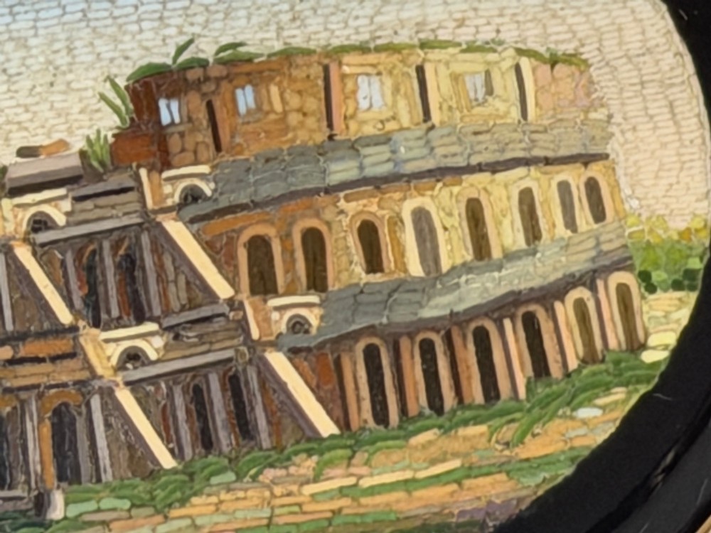 An oval nineteenth-century micromosaic brooch set in a yellow gold bezel depicting the Roman Colosseum against a light blue sky within a black surround. View V