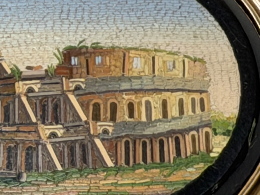 An oval nineteenth-century micromosaic brooch set in a yellow gold bezel depicting the Roman Colosseum against a light blue sky within a black surround. View VII