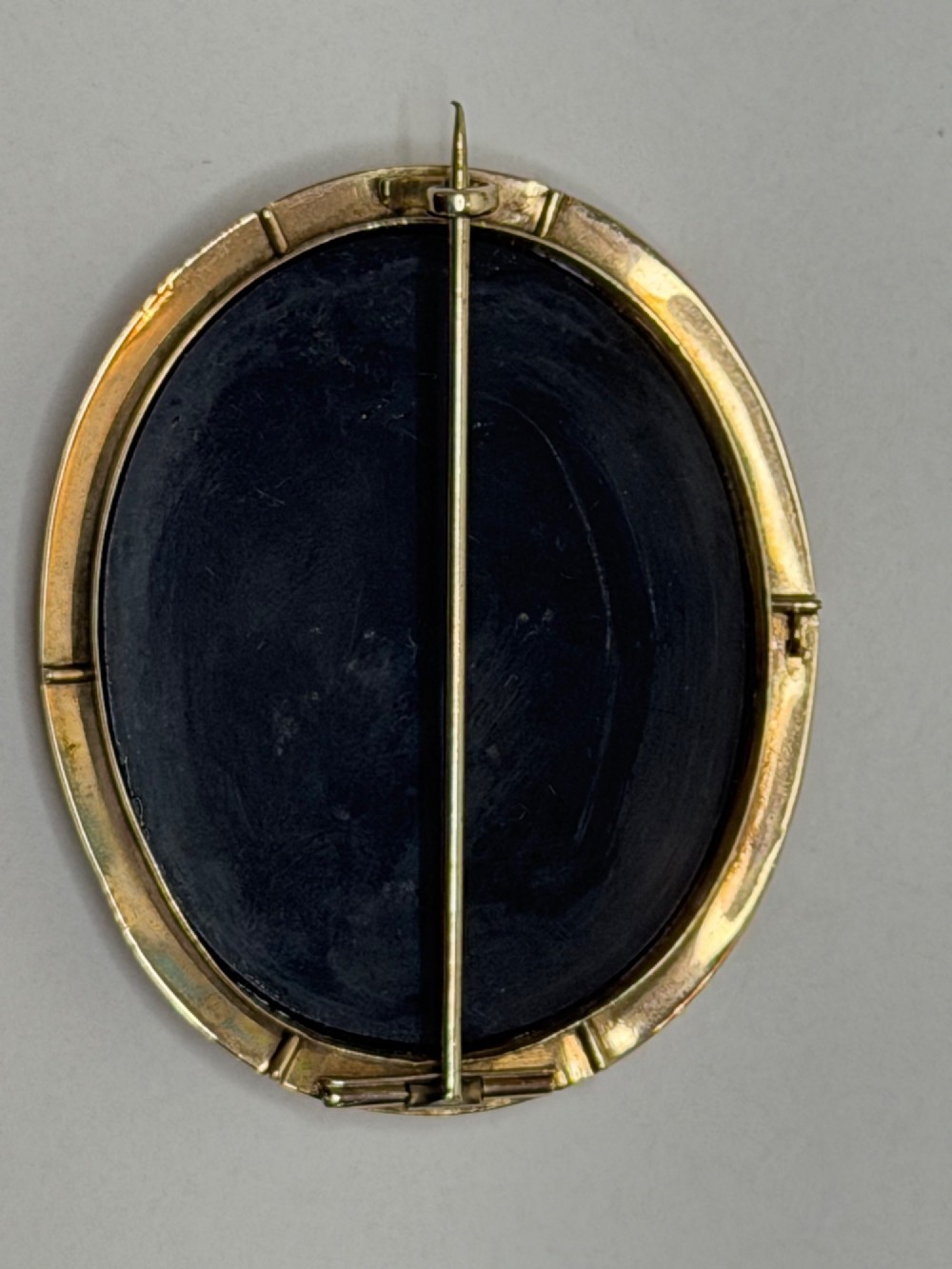 An oval nineteenth-century micromosaic brooch set in a yellow gold bezel depicting the Roman Colosseum against a light blue sky within a black surround. View XII