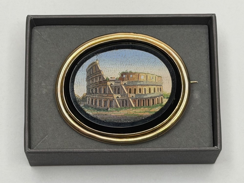 An oval nineteenth-century micromosaic brooch set in a yellow gold bezel depicting the Roman Colosseum against a light blue sky within a black surround. View XIII