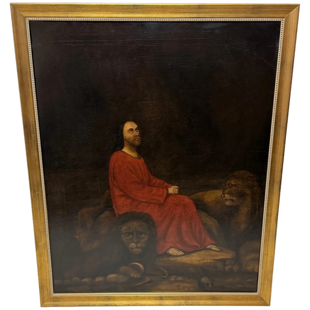 A framed Victorian oil painting depicting Daniel in a red robe seated inside a dark cavern surrounded by lions.